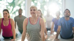 A multi-ethnic group of young adults are taking a yoga class together at the gym. They are stretching in upward facing dog.