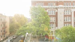 Queens, United States - September 18, 2016: In the Elmhurst neighborhood of this NYC borough an elementary school is housed in a multistory brick building. The morning sun shines brightly over residential buildings and a street lined with parked cars.