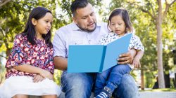 A mexican dad reads a book to his children. The young boy has down's syndrome.